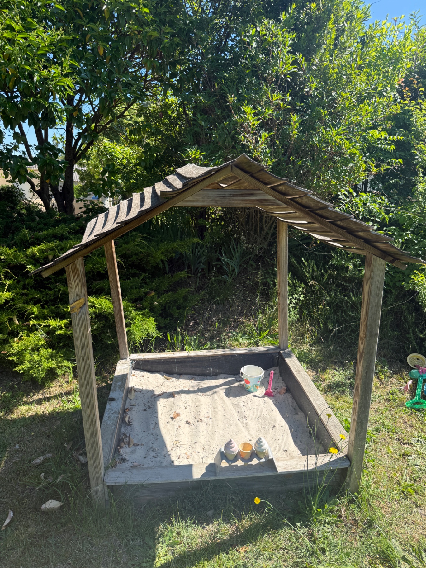 Houten zandbak met dakje en speelgoed in de tuin